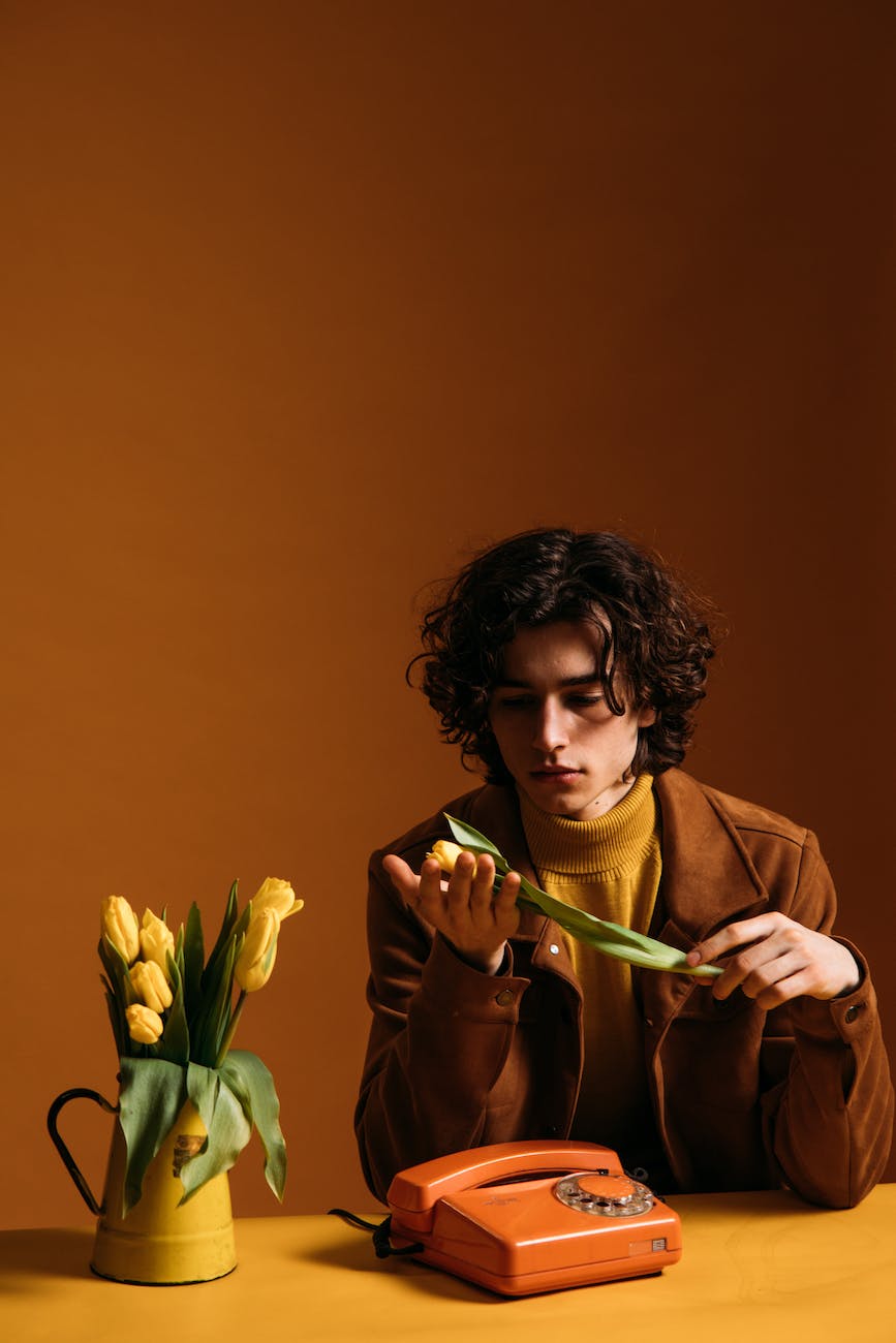 young man in brown coat holding yellow tulips